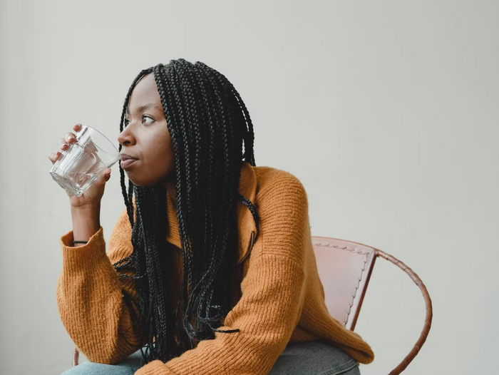 Frau mit langen Braids trinkt ein Glas Wasser und schaut dabei zur Seite.