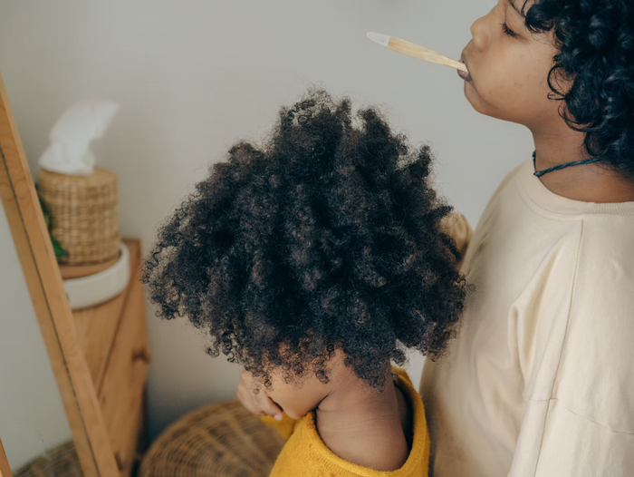 Kinder mit dichtem lockigem Haar putzen sich mit einer Bambuszahnbürste die Zähne