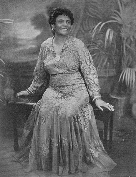 Historisches Schwarz-Weiß-Portrait von Sara Spencer in einem gemusterten Kleid, die auf einem Stuhl sitzt.