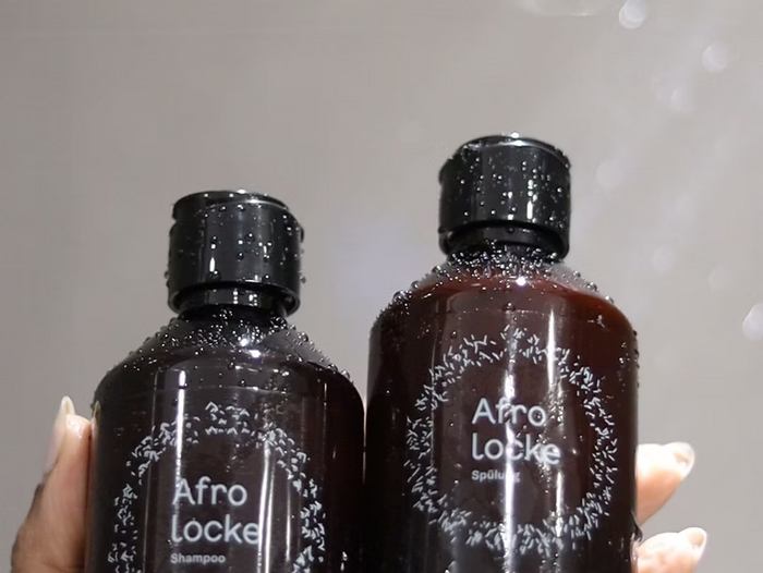 Hand hält eine Flasche Afrolocke Shampoo und eine Flasche Afrolocke Spülung