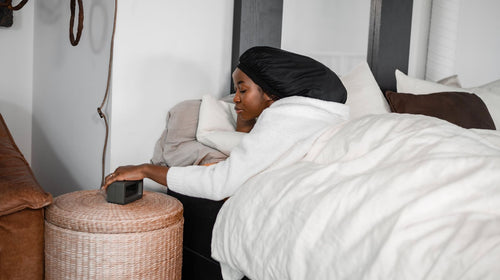 Frau mit Satin-Bonnet liegt im Bett und schützt ihre Locken über Nacht
