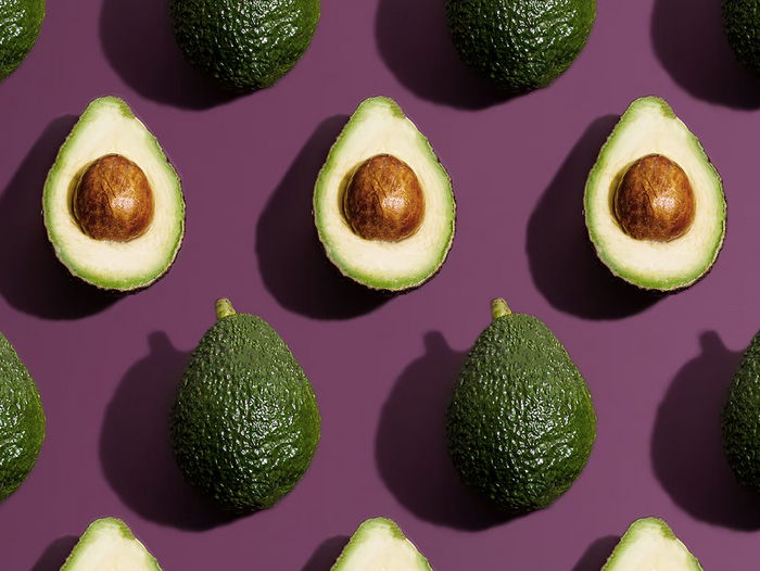 Mehrere ganze und halbierte Avocados in einem regelmäßigen Muster auf lila Hintergrund