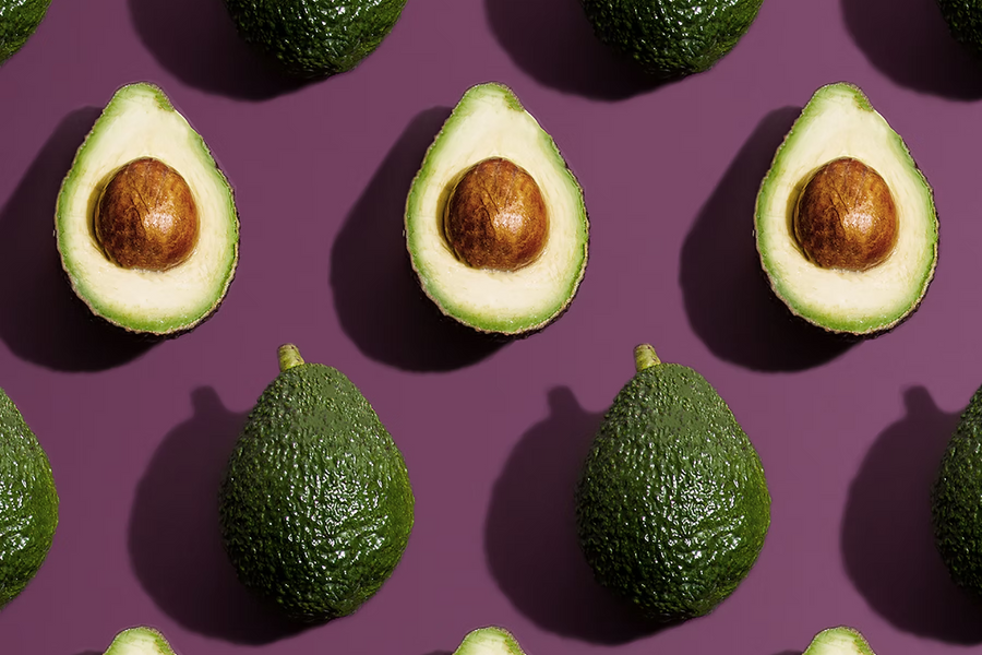 Mehrere ganze und halbierte Avocados in einem regelmäßigen Muster auf lila Hintergrund