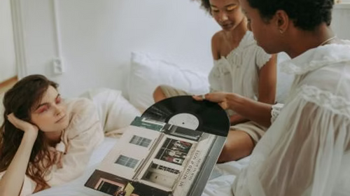 Drei Personen auf einem Bett schauen sich gemeinsam eine Vinyl-Schallplatte an.