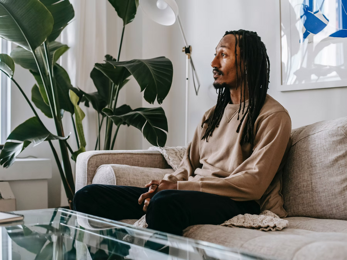 Mann mit Dreadlocks sitzt auf einem Sofa in einem hellen Wohnzimmer