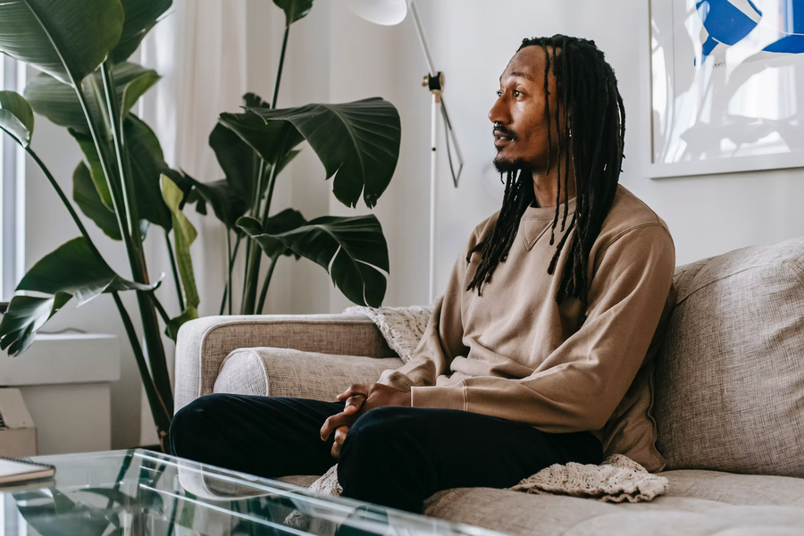 Mann mit Dreadlocks sitzt auf einem Sofa in einem hellen Wohnzimmer